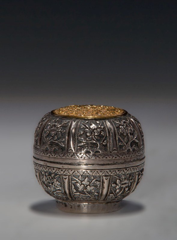 A carved silver-gilt box and cover, 19TH CENTURY: 19TH CENTURY Metallic surface with a silver even tone. Overall item is decorated with flower blossoms. The top cover of the box is also garnished with flower blossoms but in golden gilt tone. The base