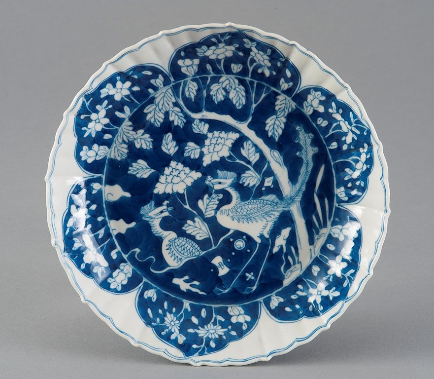 A BLUE AND WHITE PHOENIXS DISH: KANGXI PERIOD The bowl has a blue- and white colour tone overall. The interior of the bowl is decorated with a two phoenixes face to face surrounded by numerous flowers and blossoms. The exterior is g