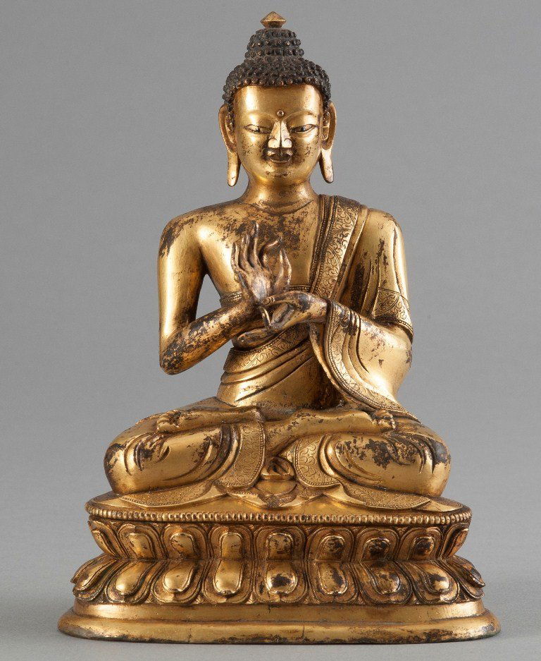 A GILT BRONZE BUDDHA: Seated in dhyanasana on a double-lotus base with the hands in bhumisparsamudra, clad in a diaphanous sanghati with beaded hems, the face with serene expression centered by a raised urna and flanked by