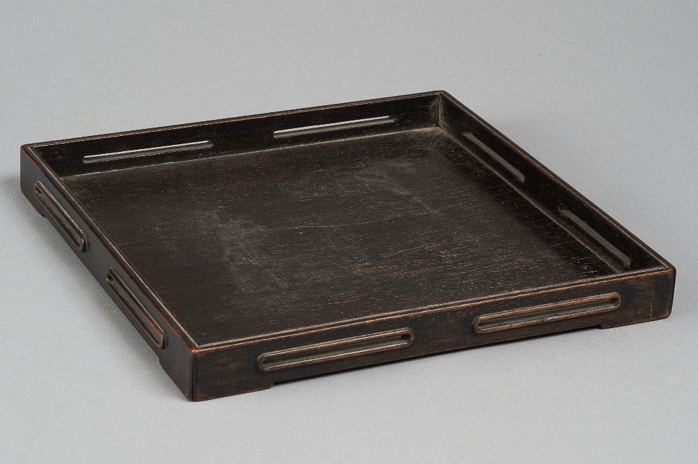 A ROSEWOOD TRAY: 19TH CENTURY The tray is square- shaped, each edge of the tray has two equal rectangular gaps. The tray is dark- brown colour tone overall. 11 1/4 in. (28.6 cm) long, 11 1/4 in. (28.6 cm) wide, 1 1/8 