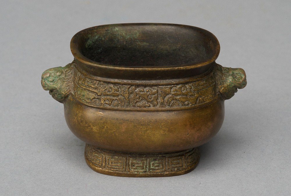 A SMALL BRONZE CENSER WITH MASK-FORM HANDLES: 18TH CENTURY The censer is a dark- brown colour tone overall, of wide globular- shaped. The exterior of the censer is decorated with layers of imperial design. The two attached handles is a face of a 