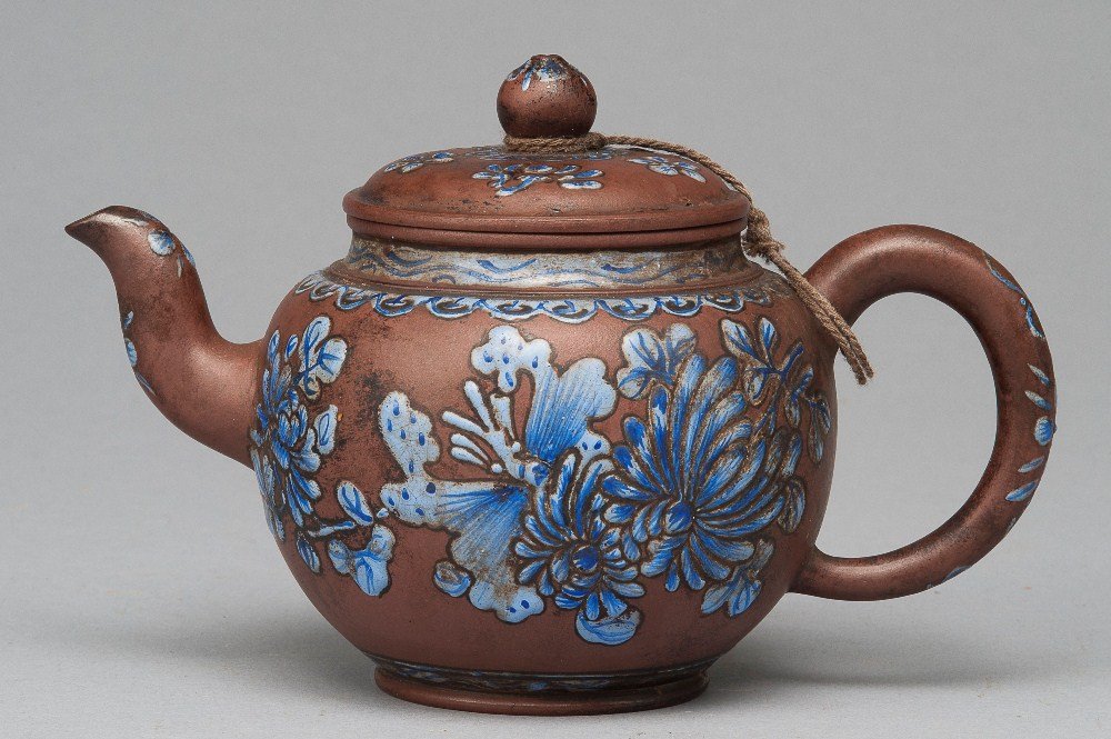 A PAINTED YIXING TEAPOT: 19TH CENTURY The teapot is a light brown colour tone overall. The exterior of the teapot is garnished with numerous blue flower sprays. The base of the teapot is a marked seal. 5 1/4 in. (13.3 cm) tal