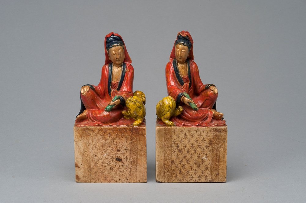 A PAIR OF SOAPSTONE GUANYIS: 19TH CENTURY The figures well carved from stone of milky olive tone and shown seated atop matching rectangular soapstone bases with their robes gathered gracefully around their bodies, the soft oval f