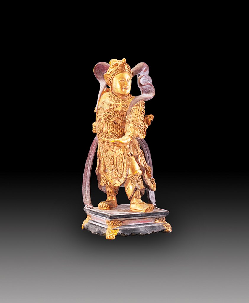 A GILT-LACQUERED WOOD FIGURE OF THE KING-GUARDIAN: EARLY 20th CENTURY The erected figure is wearing military armor and helmet and surrounded by a ribbon. 15 1/4 in. (38.7 cm) tall.