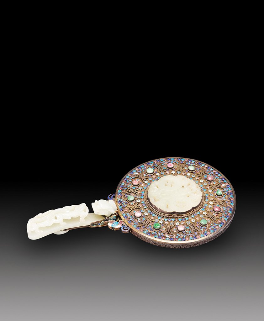 A SILVER ENAMEL AND PRECIOUS STONE INLAID WHITE JADE: 18th CENTURY The mirror is circular- shaped inlaid with colorful stone, the handle is a carving of a dragon. 5 3/16 in. (13.2 cm), 9 1/16 in. (23 cm).