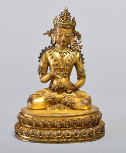 A GILT BRONZE FIGURE OF VAJRASATTVA: MING DYNASTY Seated in dhyanasana on a double-lotus base with a vajra held to his chest and a ghanta in his lap, clad in a close fitting dhoti with incised hems and beaded jewelry , the serene face su