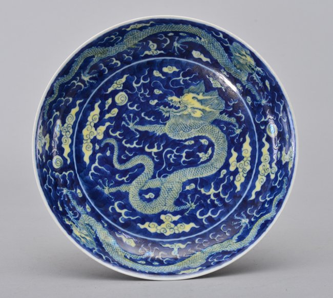 A BLUE-GROUND -YELLOW-GLAZED DRAGON DISH: Mark And Period Of KangXi The dish is of concave-shaped and the interior is decorated with a single dragon in the center surrounded by ruyi clouds and mists. The border of the dish is decorated with t