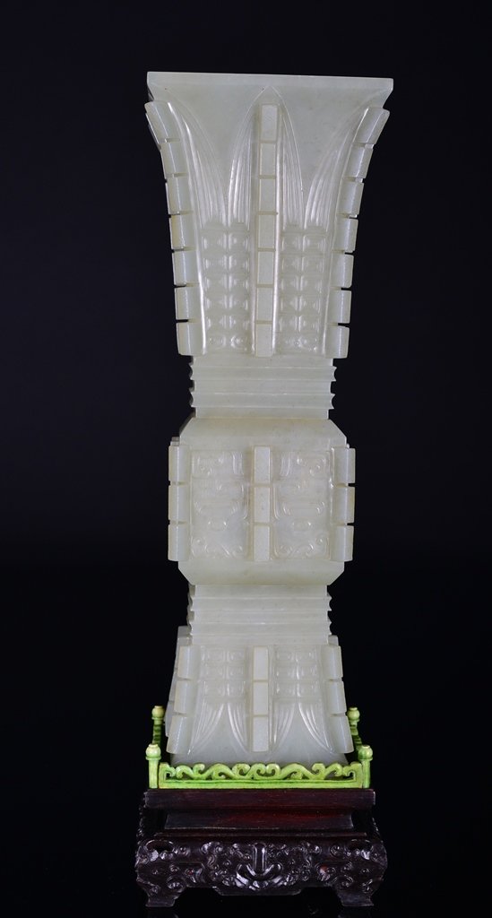 A CARVED WHITE JADE 'BANANA LEAF' BEAKER VASE AND STAND: The vase is cylinder-shaped, the exterior is decorated with numerous imperial and ruyi design. The vase is also supported by wooden square-shaped stand. 11 7/8 in. (30.1 cm) tall without stand.