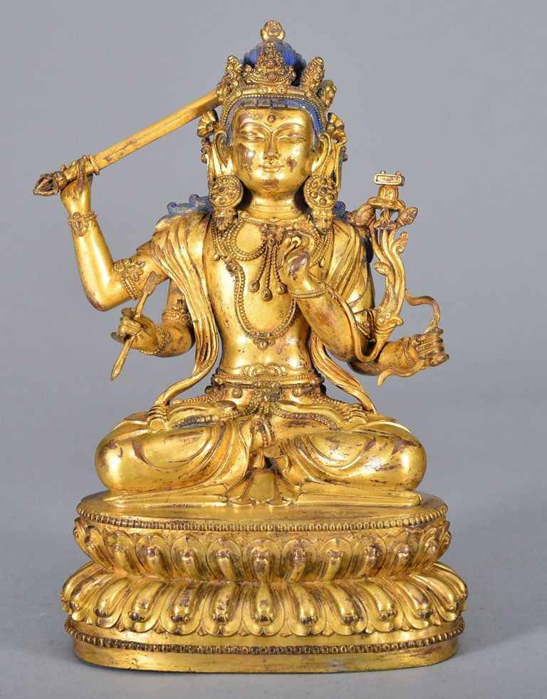 A GILT BRONZE FIGURE OF MANJUSHRI: Ming period Finely cast seated in dhyanasana on a double lotus base, holding a sword and arrow in his right hands, his left hands holding a bow and performing shri mudra while holding a lotus stem