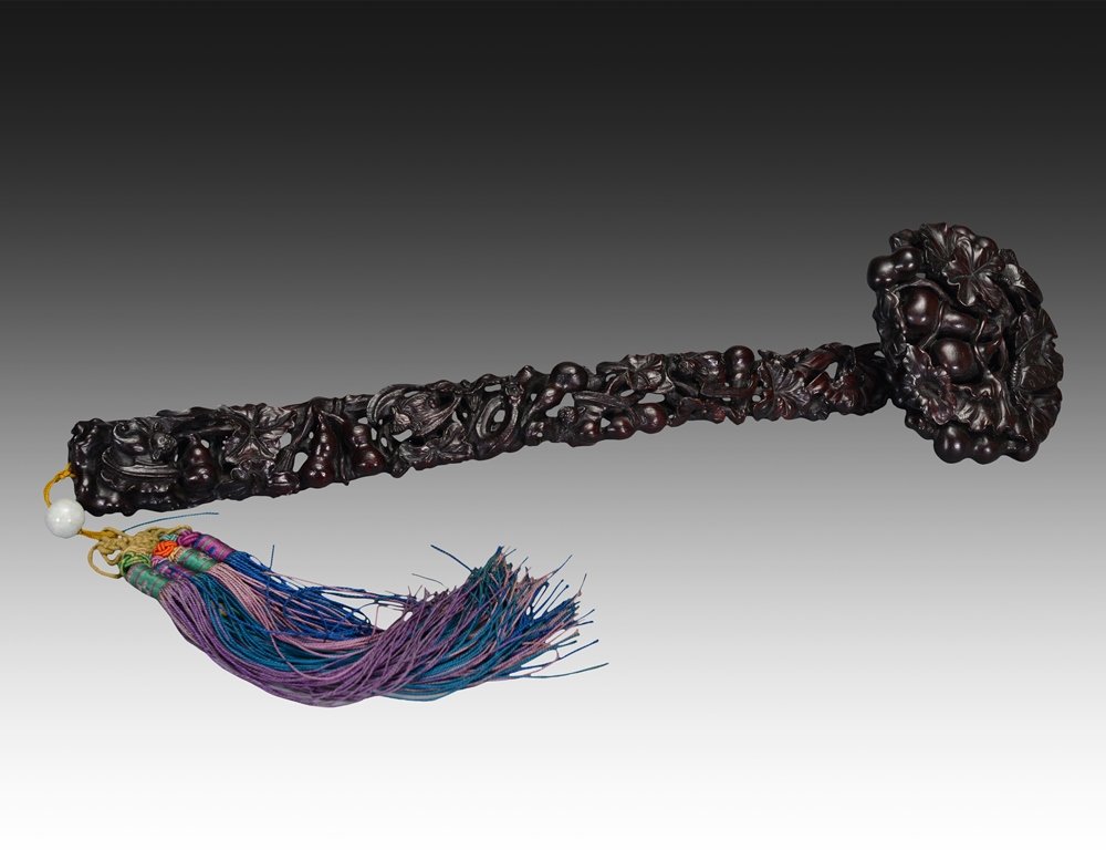 A CARVED ZITAN RUYI SCEPTER: The scepter is long and black color tone. The handle of the scepter is decorate with various imperial designs, roots and blossoms. 13 5/16 in (34.6 cm) long.