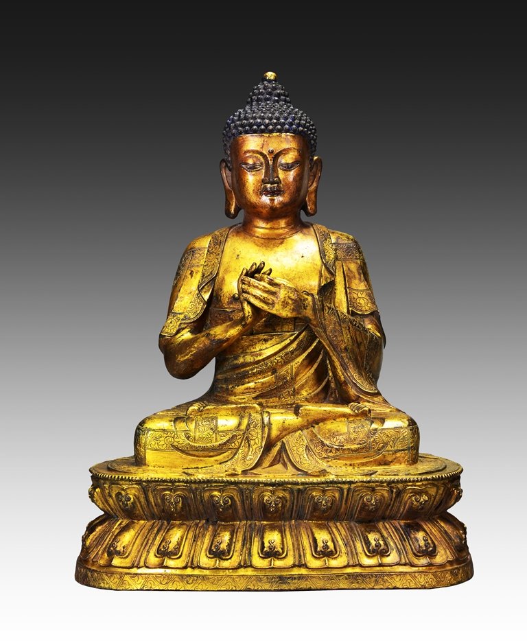 A LARGE GILT BRONZE FIGURE OF BUDDHA: Ming Dynasty Seated in dhyanasana on a separately cast double lotus base, with his hands in the gesture of teaching, his sanghati loosely draped over his left shoulder falling in crisp folds and dec