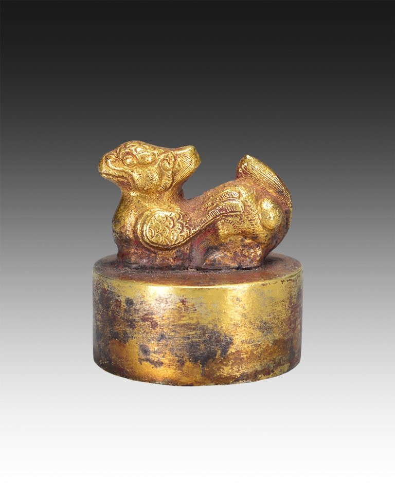 A CARVED GILT BRONZE SEAL: Han Dynasty The seal is irregular concave-shaped. The exterior is decorated with an animal standing on a circular base. The seal is bronze color. 1 11/16 in. (4.3 cm) tall.