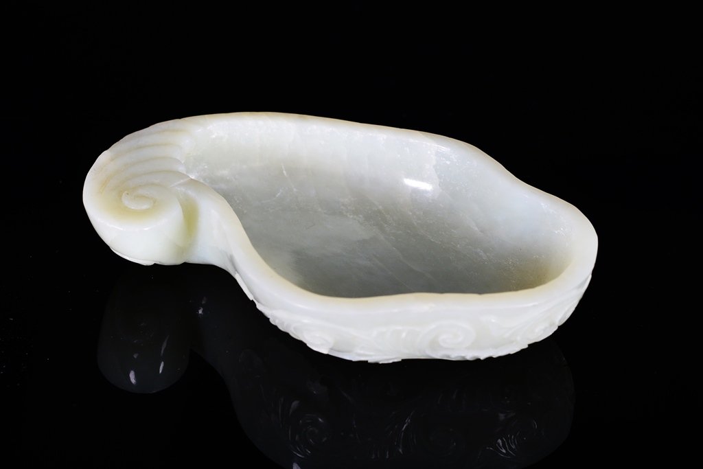 A CARVED WHITE JADE WASHER: The washer is concave-shaped. The exterior is decorated with little imperial designs and some ruyi clouds. The washer is white jade color. 4 3/8 in. (11.1 cm) wide, 15/16 in. (2.3 cm) tall.