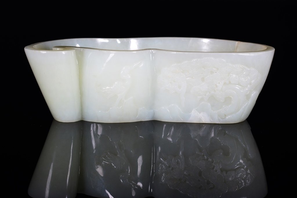 A CARVED WHITE JADE WASHER: The washer is concave-shaped. The exterior is decorated with animals surrounded by trees. The washer is white jade color. 5 7/16 in. (13.8 cm) long, 1 5/8 in. (4.2 cm) tall.