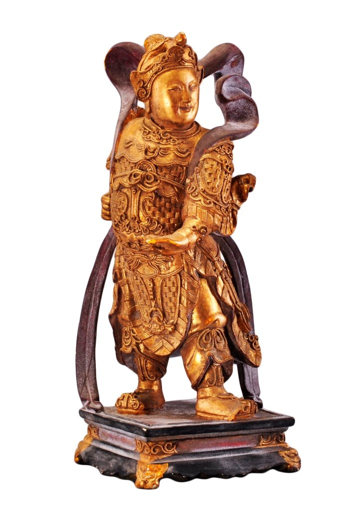A GILT-LACQUERED WOOD FIGURE OF THE KING-GUARDIAN: The erected figure is wearing military armor and helmet and surrounded by a ribbon. 15 1/4 in. (38.7 cm) tall. Early 20th Century