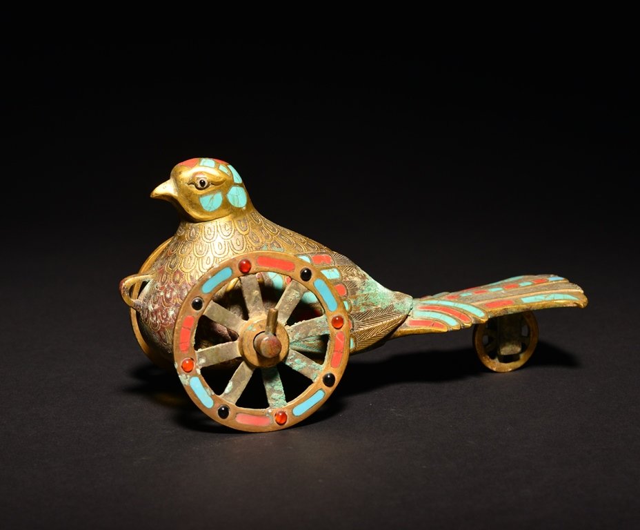 A BRONZE GEM-STONE INLAID PIGEON: The pigeon is on a wheel and decorated with colorful beads. 7 1/16 in. (18 cm) long, 3 1/2 in. (8.9 cm) tall. Han Dynasty