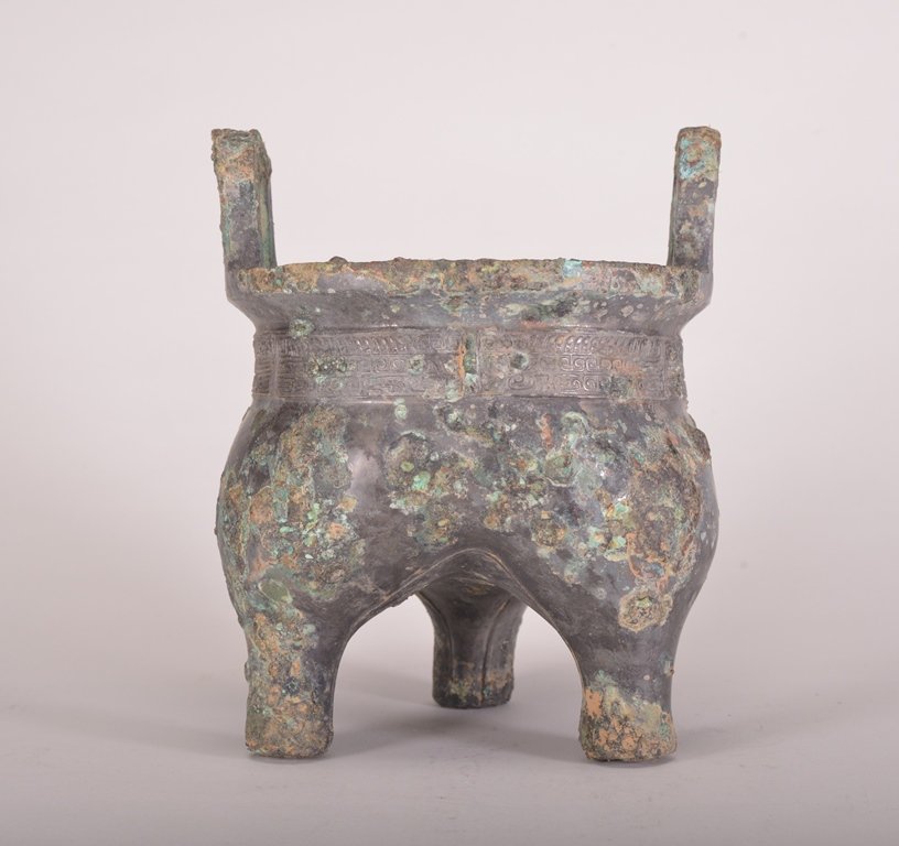 AN ARCHAIC BRONZE RITUAL FOOD VESSEL: The food vessel has a tripod legs and the exterior is decorated with imperial designs. Shang Dynasty 8 1/4 in. (21 cm) tall, 6 3/4 in. (17.1 cm) wide.