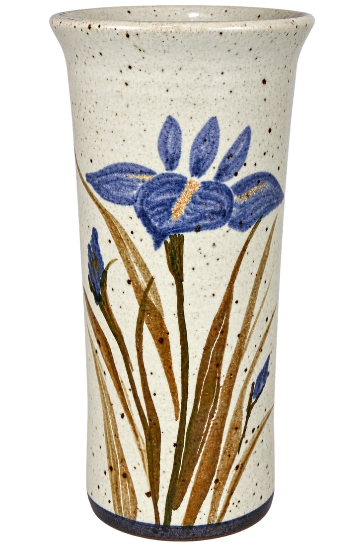 Hand-Painted Glazed Studio Pottery Vase – Blue Iris Floral Motif, 6.5”: This charming hand-painted glazed studio pottery vase features a tall cylindrical form decorated with a bold blue iris floral motif. The flower is surrounded by elongated stems, leaves, and smaller bu