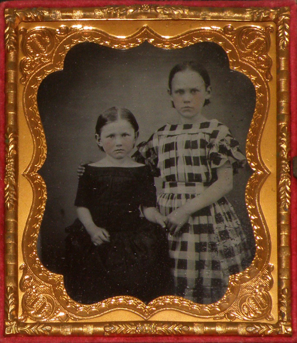 CASED 1/6 PLATE AMBROTYPE OF TWO LITTLE GIRLS: Girls have hand tinted pink cheeks, girl with checked dress has some minor scratching to right side of dress, unusual Union Case with detailed seashell on both sides, couple of corners have some minor