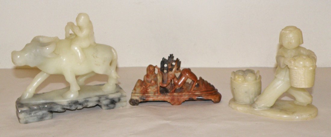 THREE CARVED SOAPSTONE FIGURES WITH PEOPLE: Peasant on water buffalo with flute, peasant girl moving produce and an elder with a deer. Minor surface abrasions. Size: Largest: 5"