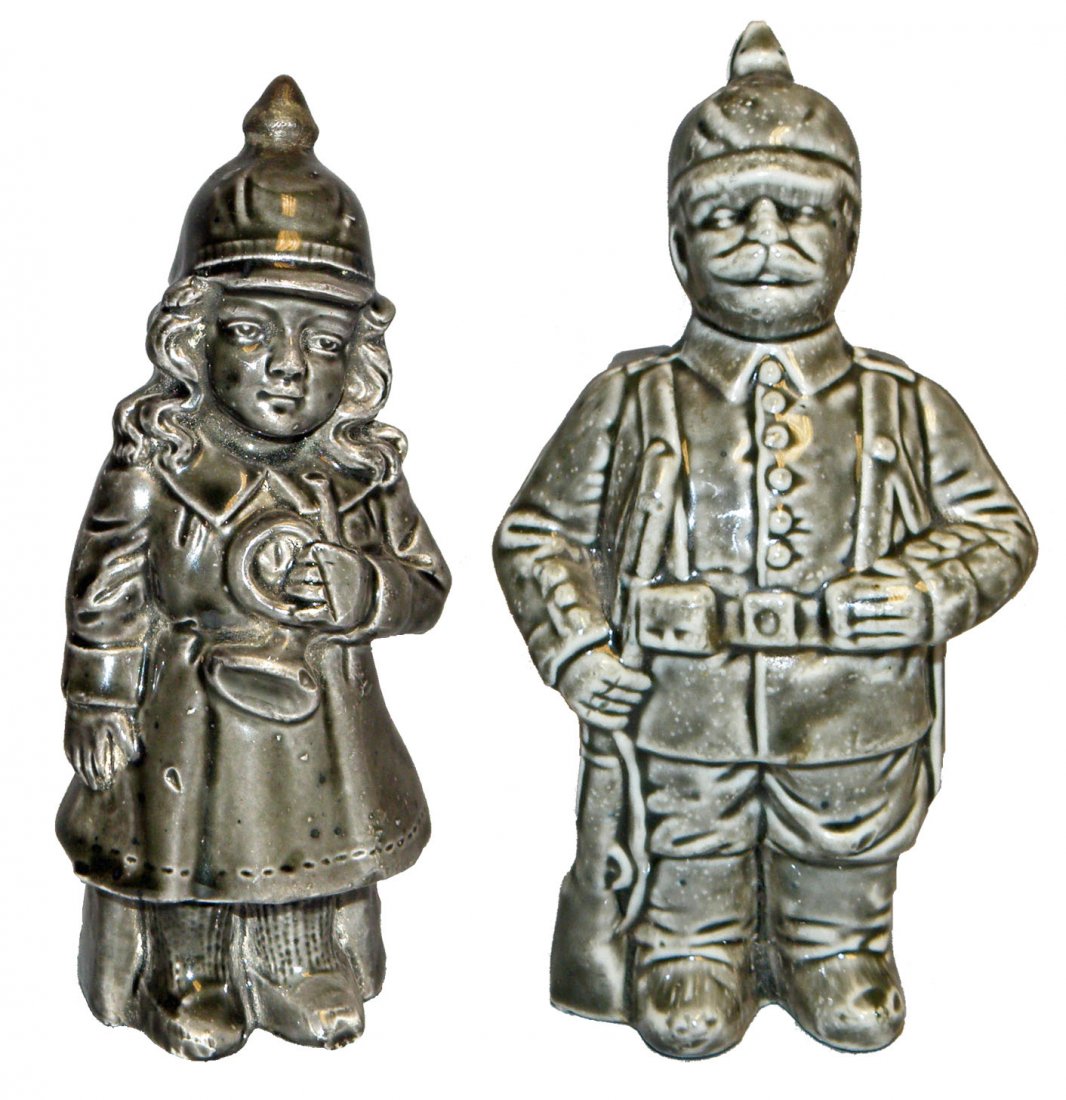 PRUSSIAN SOLDIER AND GIRL WITH TRUMPET PORCELAIN ST: Both wearing Pickelhaubes, back of man has incised number 6664, C-1914. Girl has restoration to lower back of bank. Ref. One Hundred Years of Ceramic Money Banks, by Beth Baddeley Huebner, Vol. 1, Pla