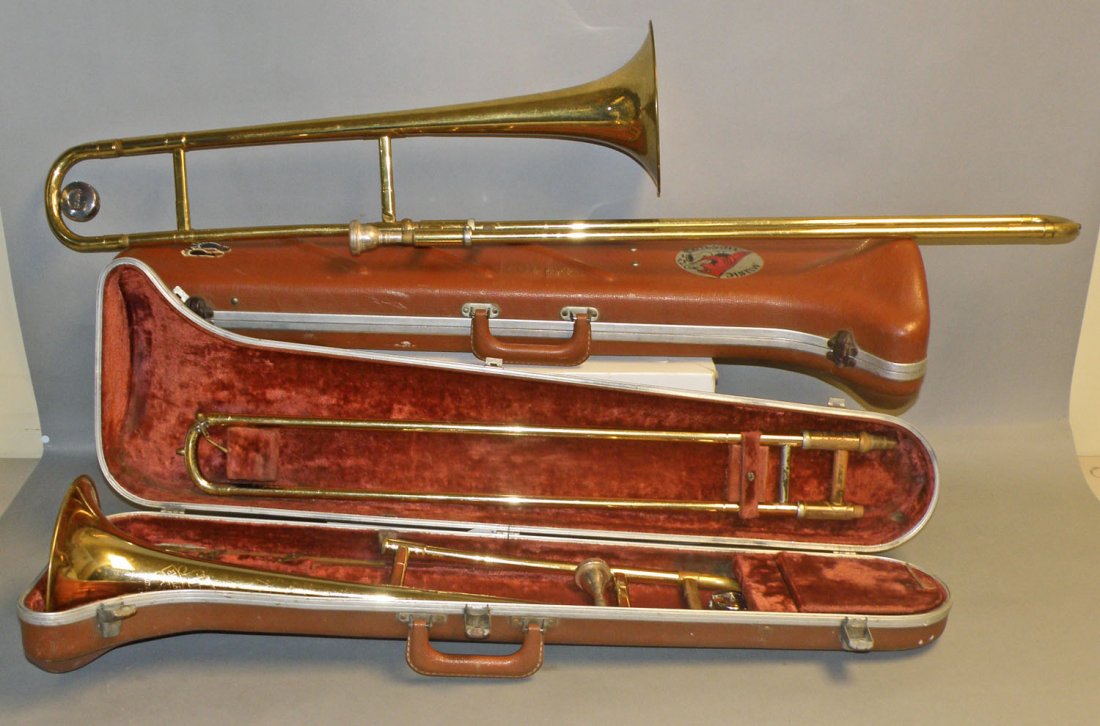 TWO CASED OLDS TROMBONES: Both are complete with mouth pieces. One retains music stand. Both show some minor dings and scuffing. Original cases Good-VG. Size: Largest 46" long