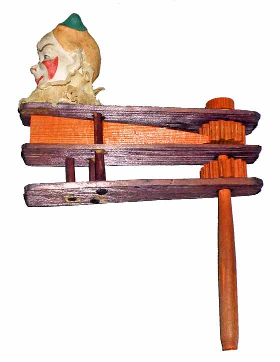 FIGURAL NOISE MAKER: Late 19th century wood noise maker. With bisque clown head. Has original crepe paper collar. Missing bottom clacker. 8" tall, 5" long
