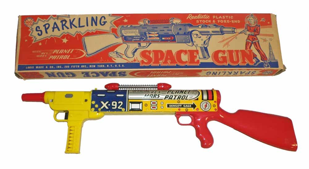BOXED MARX REX MARS SPARKLING SPACE GUN: Tin and wind-up toy works perfectly. Original box is missing one flap from inner end. Light creasing to box. Box grades very fine to excellent. 21-1/2" long