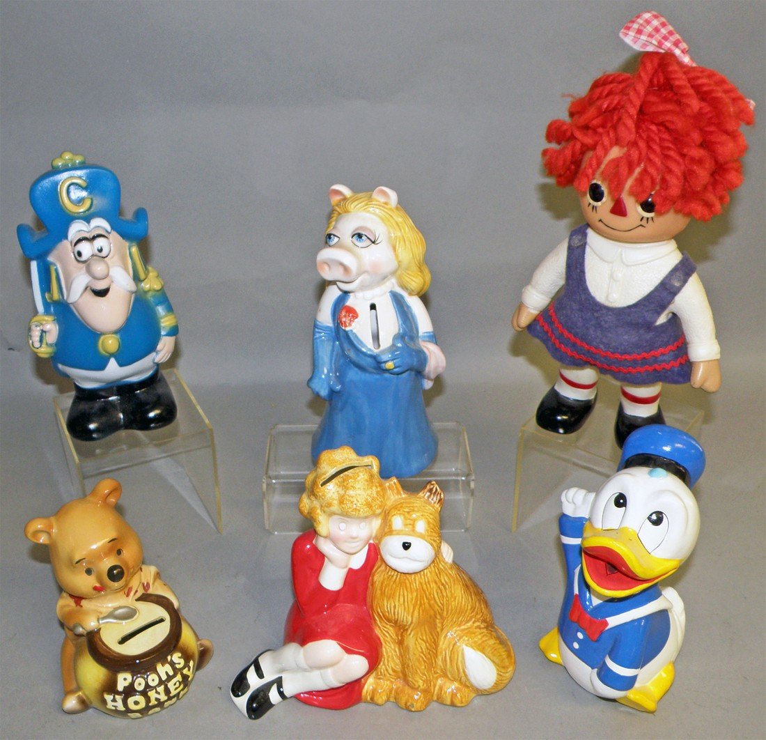 A LOT OF COMIC CHARACTER STILL BANKS: Composition Donald Duck, Ceramic Annie, Miss Piggy and Pooh and a plastic Captain Crunch and Raggedy Ann. Largest: 9" tall