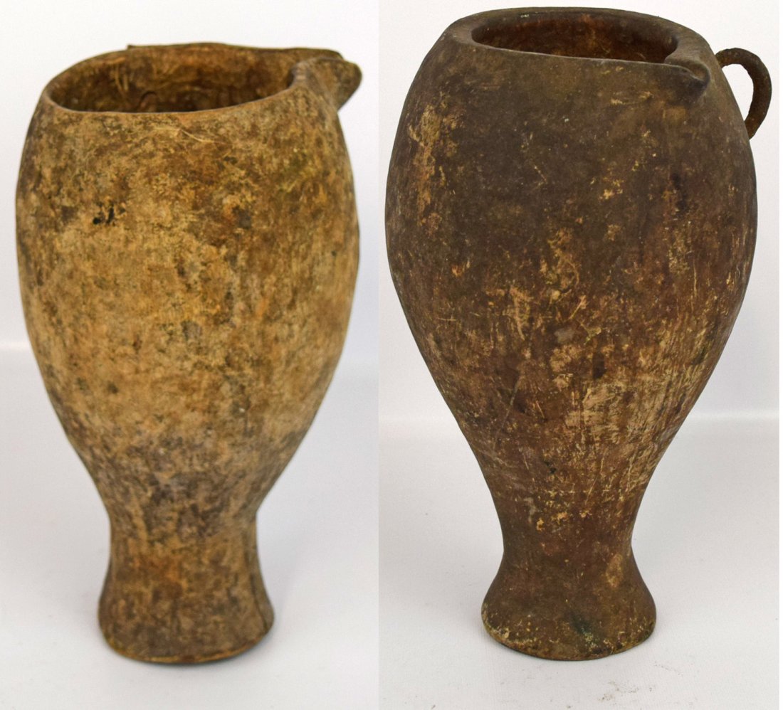 TWO KARAMAJONG MILKING JARS: Carved wood vessels with pouring spout. Used to hold mixture of milk and cow blood. Both show age and use wear 11'' tall