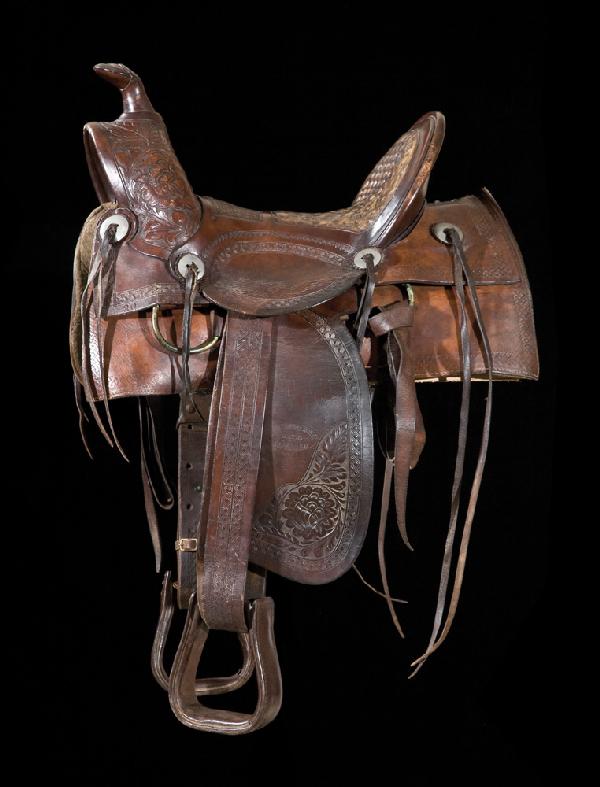 Tracy Roberts Hdw Co., Carlsbad, N.M.: Extremely rare example of an early 1900s New Mexican saddle. Slick fork, high back, basket and floral carved, eight slotted conchos with latigo strings. Very good condition.