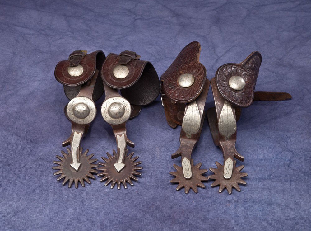 2 Pair of Crockett Spurs: a) #341 Spurs similar to the "Ben Johnson Special" without the tapered band. 1" band with single leaf overlay. Marked under the swinging button. Quality pressed floral straps; b) Arrow shank design wi