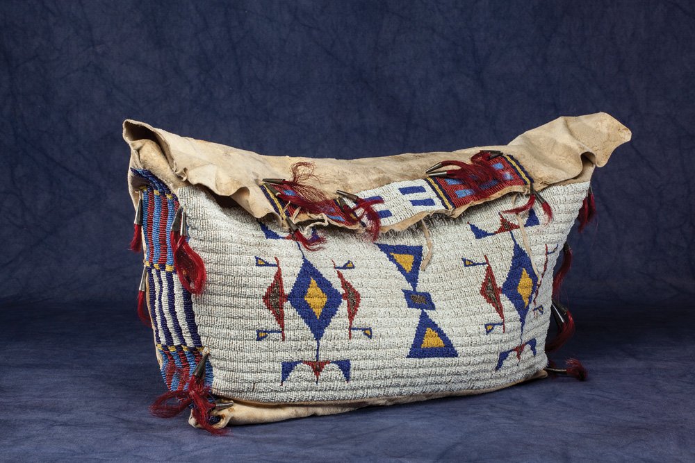 Sioux Possible Bag: 22” x 12” x 6” beaded with blue, yellow, and red geometric designs on white field. Typical bars in rectangular elements on the side panels. Tin-cone suspensions with dyed red horsehair inserts o