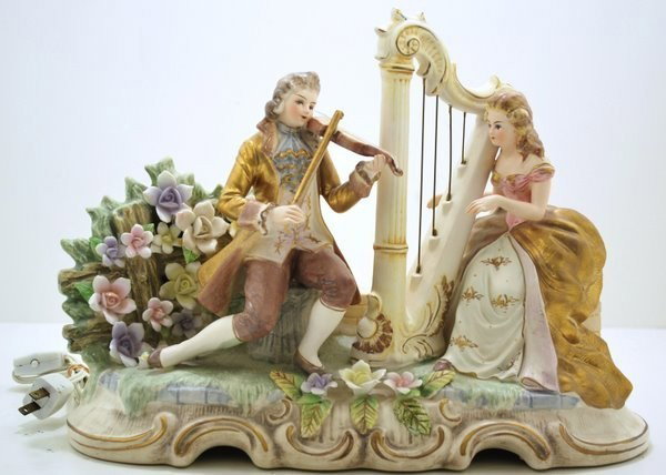 PORCELAIN LIGHTED MUSIC FIGURES: SANKYO LIGHTED PORCELAIN MUSIC FIGURES OF A MAN PLAYING A VIOLIN AND A WOMAN PLAYING A HARP, IN A GARDEN, HAND WIND MUSIC KEY.