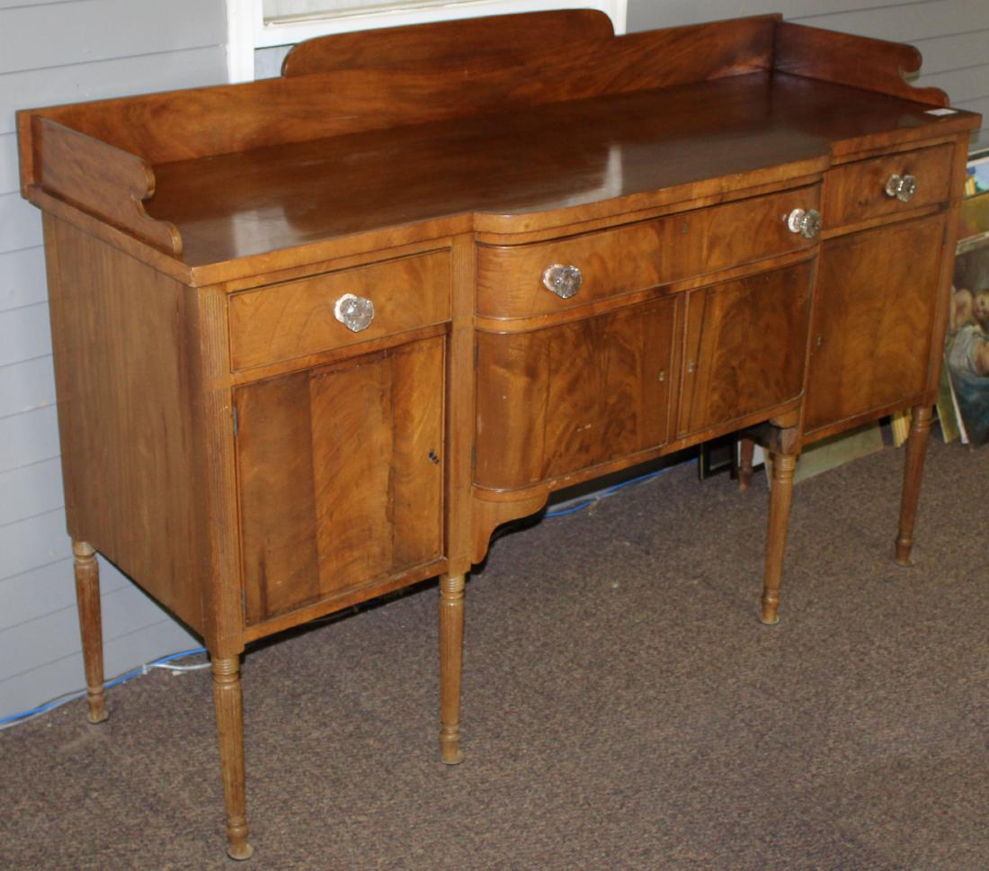 Hepplewhite mahogany reeded leg sideboard: 19th c. Hepplewhite flame mahogany reeded leg sideboard on tall reeded legs with bowed center section, 3 drawers with Sandwich glass pulls over 4 cupboard doors 48" x 26" x 72"