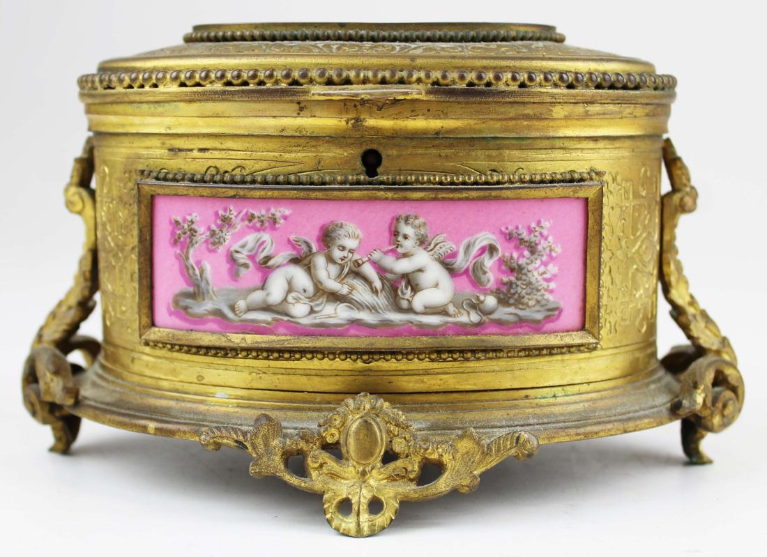 French ormolu dresser box with porcelain panels: fine French gilt ormolu brass oval dresser box inset with porcelain panels showing scenes of putti and foliage, signed Tahan (Paris) Boulevard des Italiens 4.5" x 7" x 5"