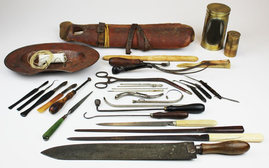 19th c surgical & medical tools: Oustanding grouping of various 18th or 19th c medical and surgical instruments including a wood leg splint in old surface, several early scalpels, early saw, knives, hooks, probes, forceps, basin, and
