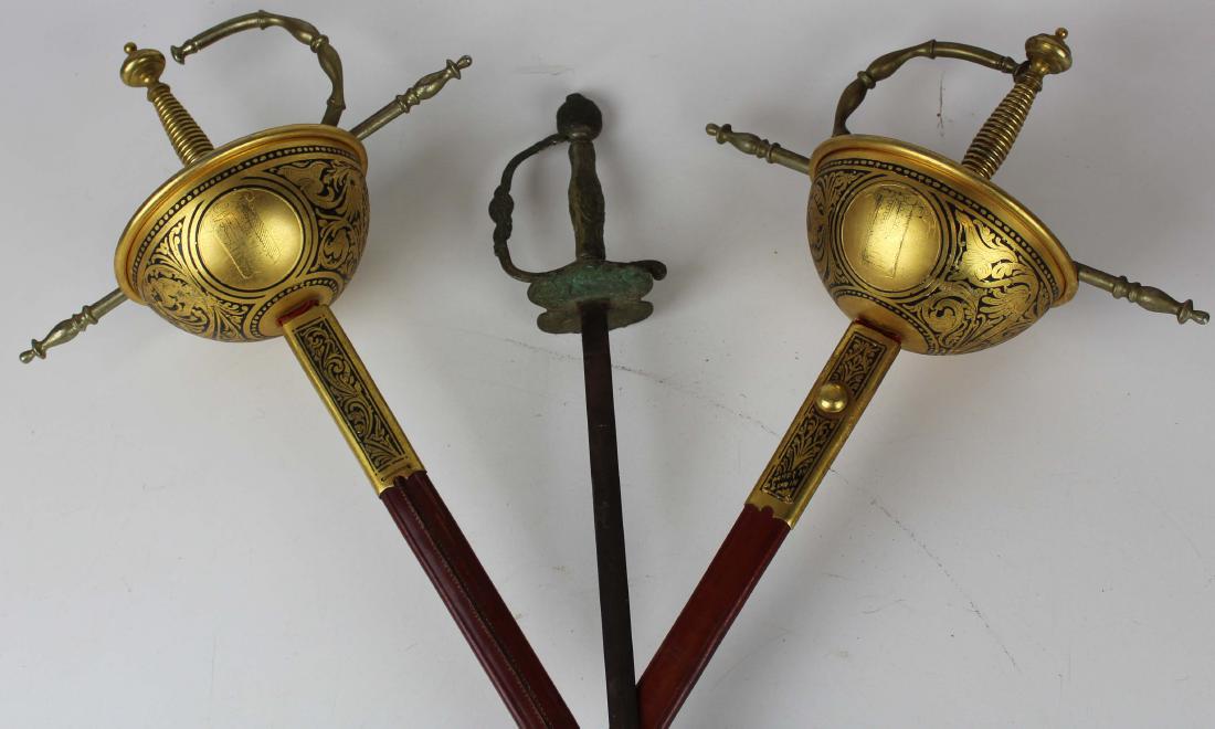 Pair of Spanish rapiers and a small sword: pair of 20th c Toledo Spain rapiers with gilt decoration, leather scabbards, 36" blades 44" overall, one sword missing tip of scabbard; Continental small sword with German silver hilt/grip with classi