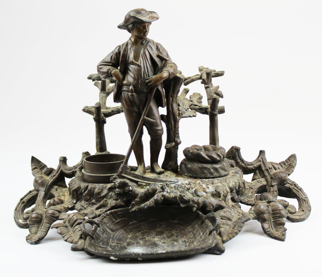 19th c white metal figural desk stand: 19th c white metal figural desk stand/ pen holder, farmer with scythe, sander & lidded ink with porcelain liner, damage to end of leaf on one foot, ht 9", width 12"