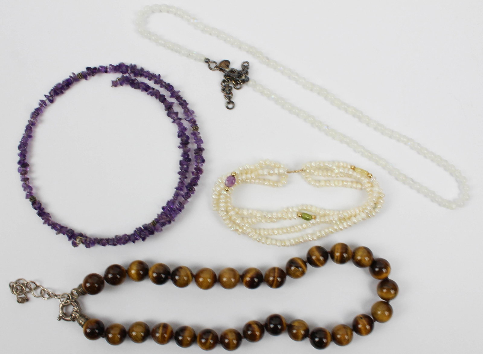 Four pieces of jewelry: A group of four pieces of jewelry including a cats eye bead necklace, a raw amethyst necklace, polished crystal necklace, and a triple string freshwater pearl and 14k yellow gold bracelet.