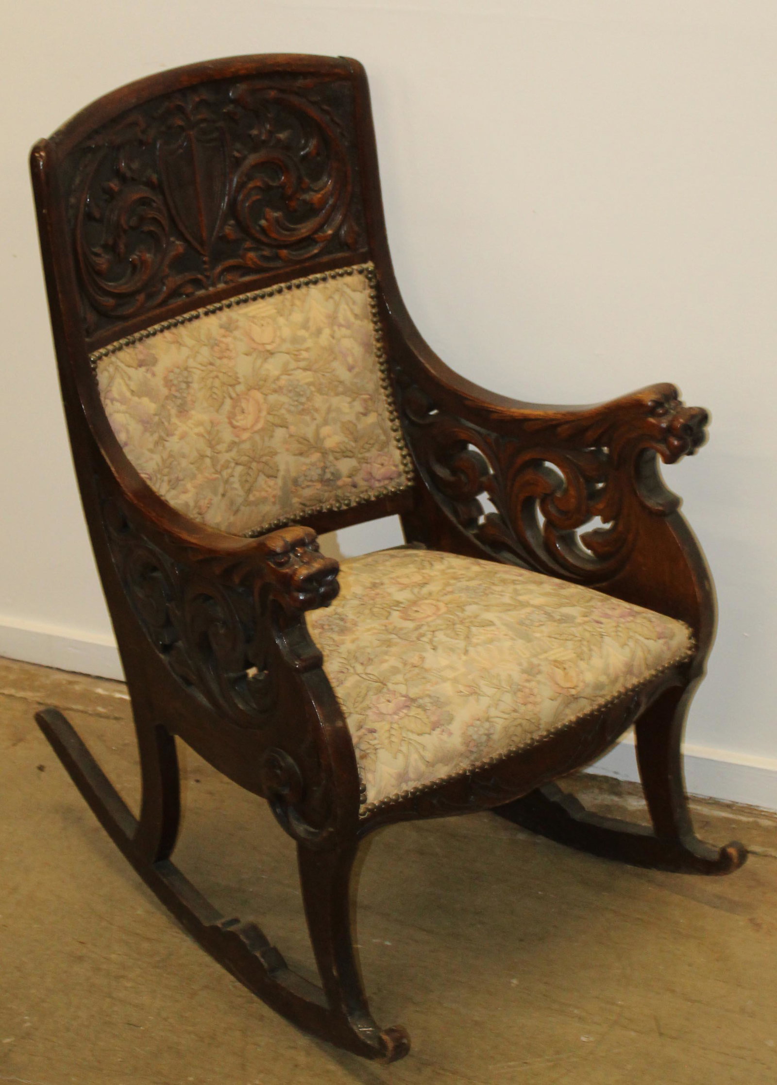 Oak carved rocking chair: Oak carved rocker. Lion's head arms, coat of arms back, upholstered seat and back.