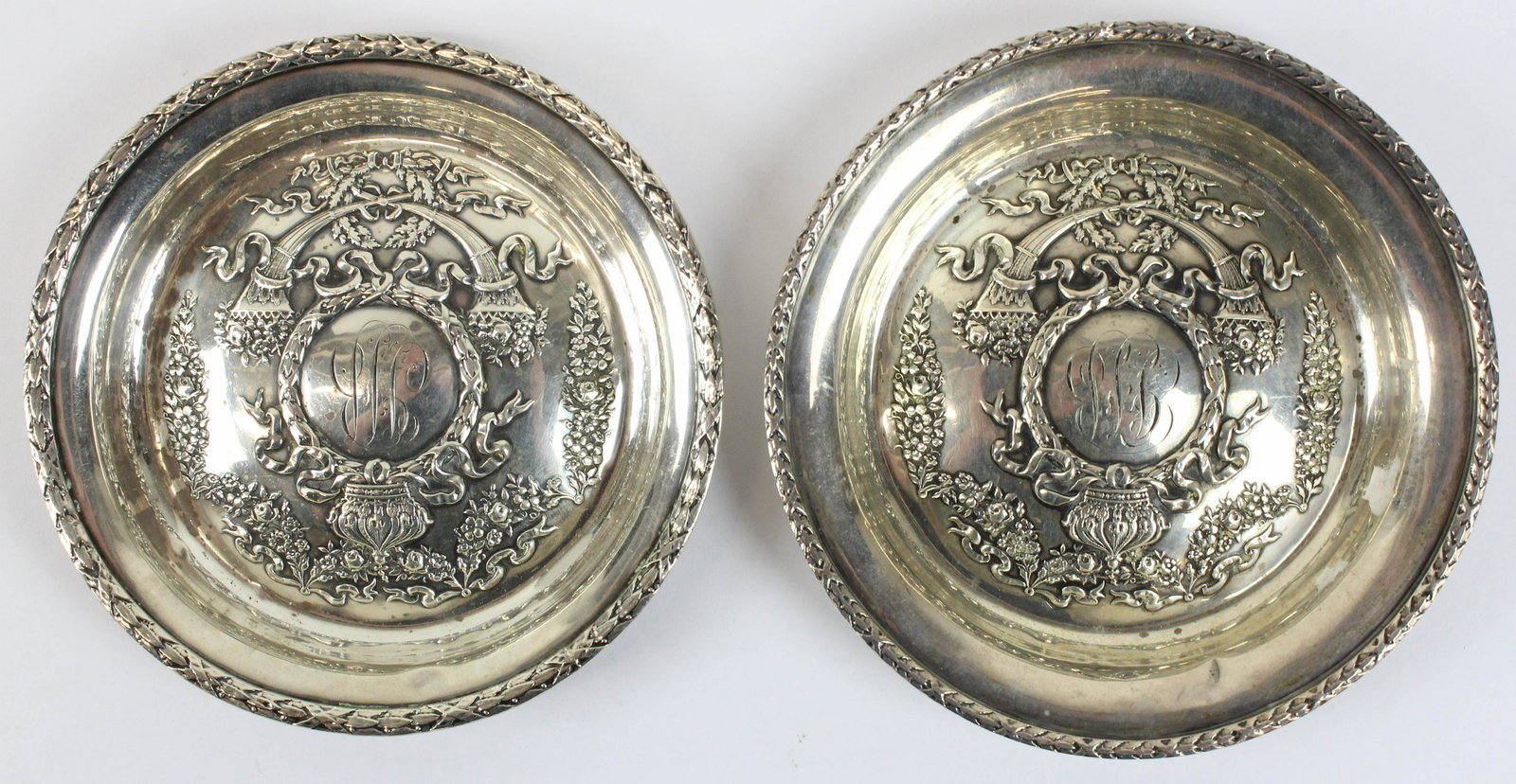 Two Durgin Empire Sterling Bottle Coasters: Two ca. 1910 Durgin "Empire" pattern sterling silver nesting bottle coasters with floral festoons and neoclassical decoration -minor dents 4.75", 5" 4.1 troy oz. weighable