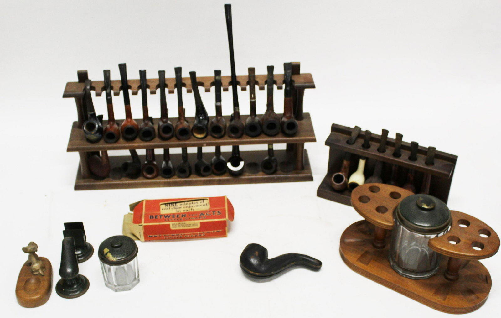 Collection of Pipes and Pipe Racks: Approximately 26 Estate pipes with pipe racks, including Kaywoody, Amphora, Brigham, De Peltier NOS store display with Between the Acts Little cigars with three unopened tins of the same