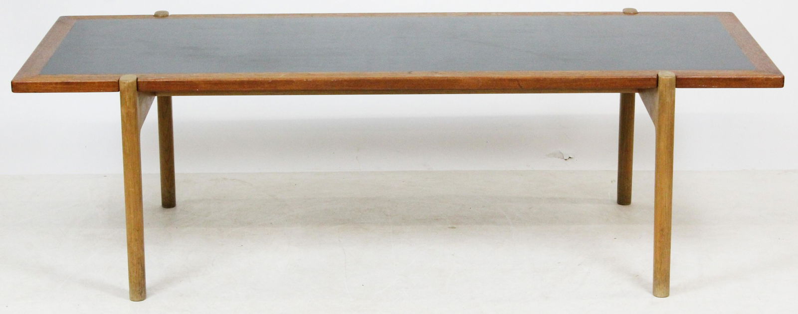 Johannes Hansen Teak Coffee Table: A signed Danish teak modern coffee table Johannes Hansen. Four peg legs, cross stretcher, Brass mounted, black laminate center top, 63" x 24" x 20" h. Sun faded base