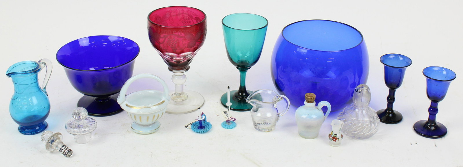 Lot of Early Colored Blown Glass Examples: Lot of early colored free blown glass examples including 2 cobalt blue flint cordial goblets, teal green goblet, cranberry cased overlay cut to clear goblet with engraved decoration, footed cobalt bow