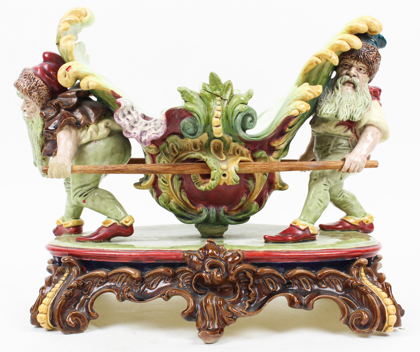 Majolica Centerpiece of Gnomes Carrying Basket: Unusual Late 19th c. European polychrome Majolica glazed figural ceramic centerpiece of two gnomes carrying basket on elaborate rococo style base 12" x 14" x 8" - repairs to rim, hands of gnomes, and 