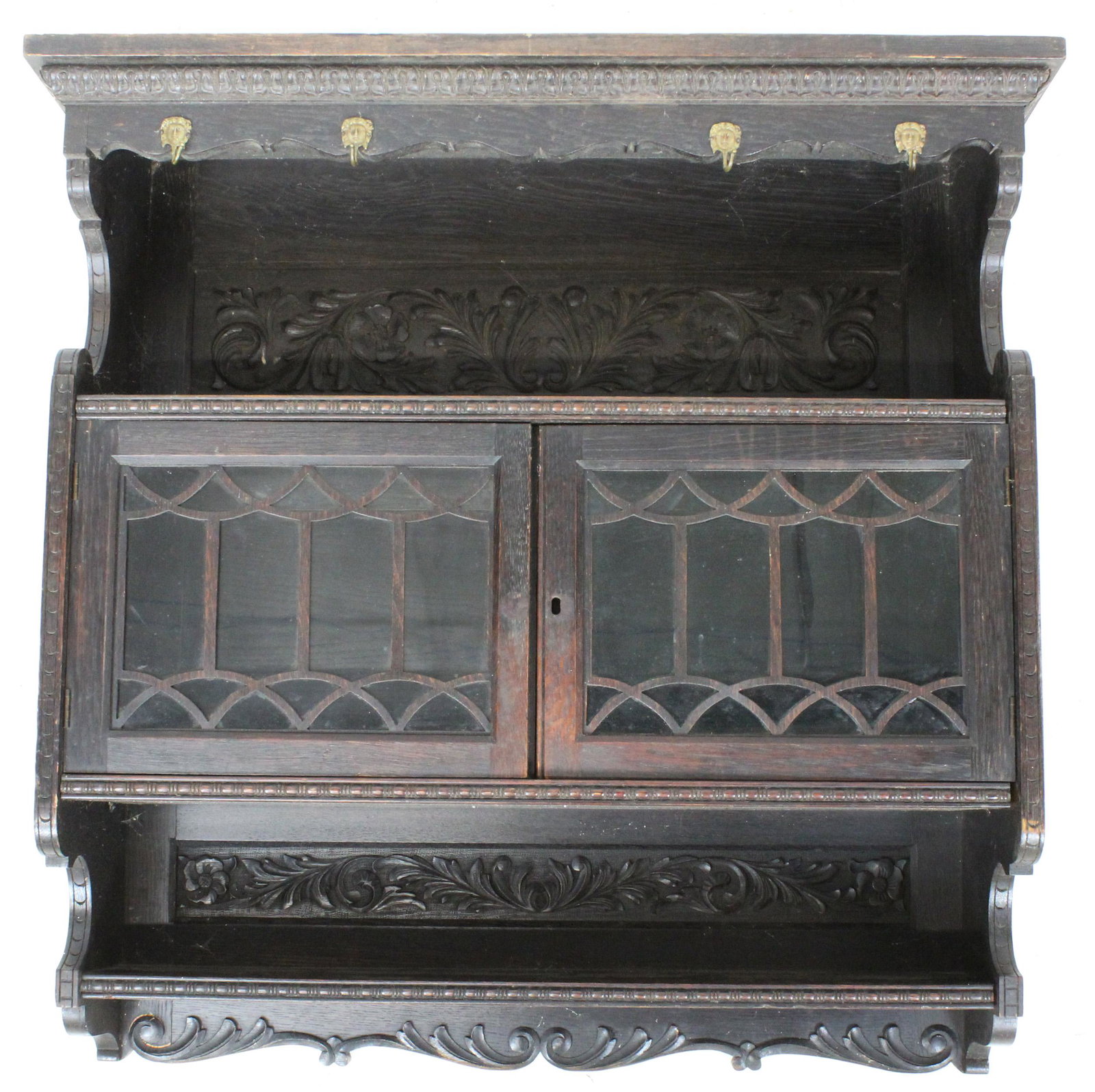 Carved European Oak Hanging Cupboard: ca. 1910 European Jacobean revival style dark stained oak hanging wall cupboard with 2 glass doors, profusely carved upper and lower panels, foliate carved ends, and female figurehead brass mug hooks 
