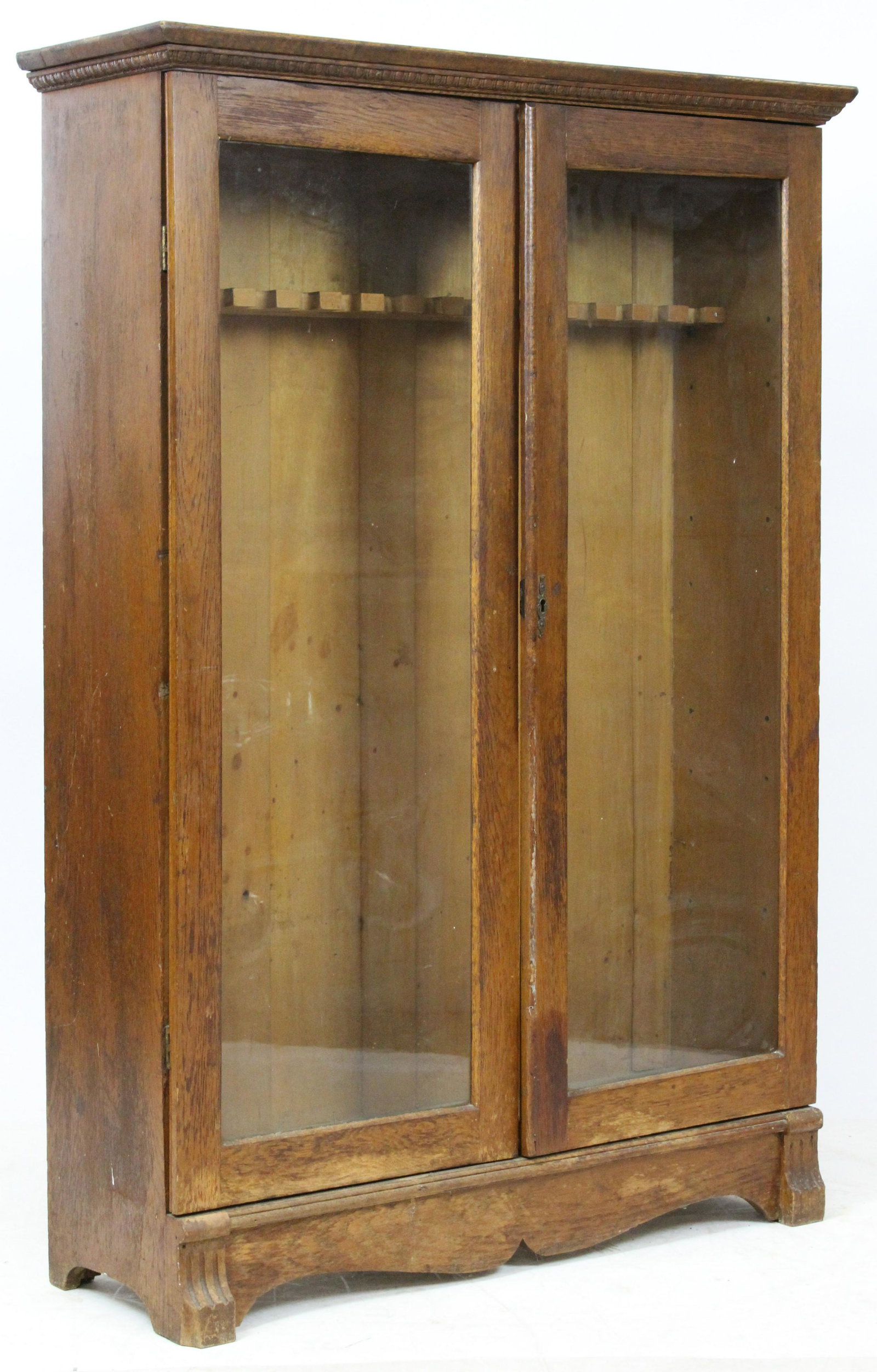 Larkin Type Oak Bookcase Converted To Gun Cabinet: ca. 1900 Larkin type oak glass double door bookcase with shelves removed and holders for long guns added, cast brass escutcheon 54" x 38" x 12" -losses to trim, wear to finish