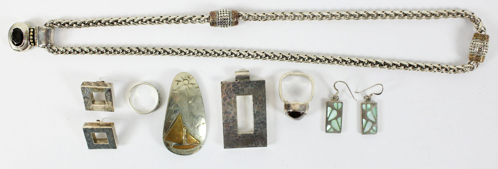 Designer Silver Jewelry: A group of designer silver jewelry including a pendant earring set, barrel necklace with onyx pendant, copper on silver pendant with sailboat, amber & silver ring, and more.
