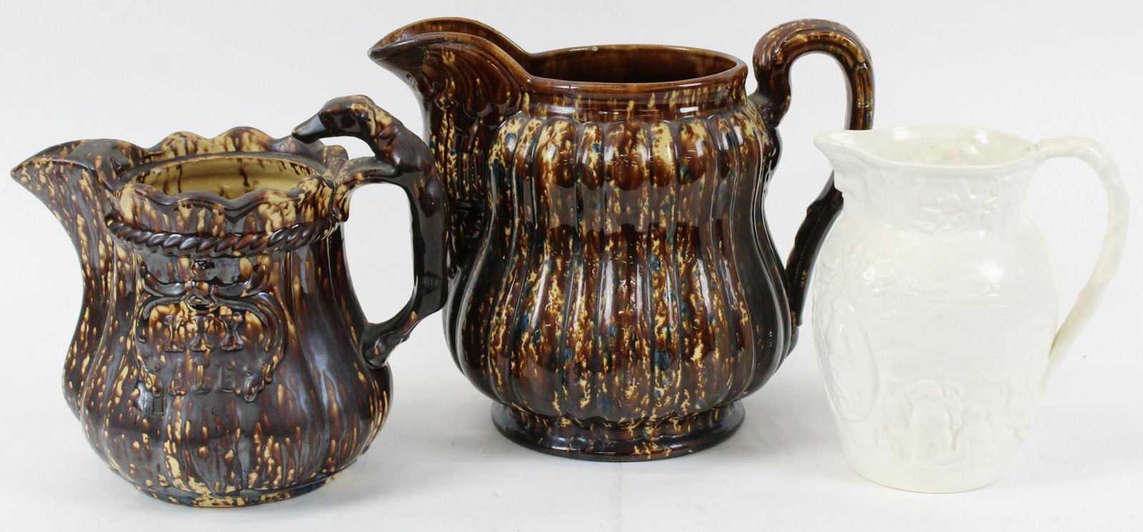 Rockingham, Bennington and Minton Pitchers: Group of 3 pottery pitchers including rare 19th c. Rockingham flint glaze hound handle ale pitcher with embossed cartouche indicating "XXX" (missing lid), oversized ribbed pitcher with Bennington coba